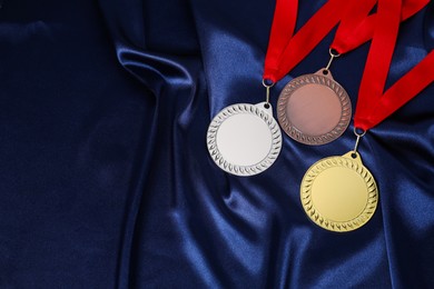 Photo of Golden, silver and bronze medals on blue fabric, top view. Space for text