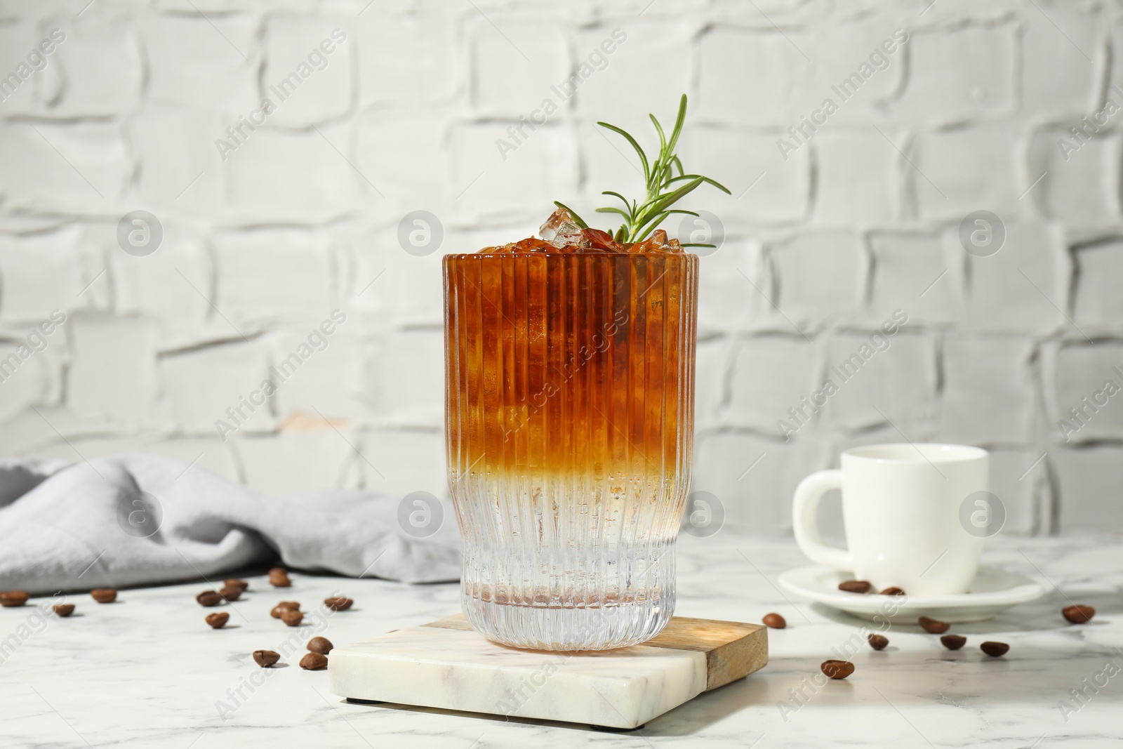 Photo of Refreshing espresso tonic drink with rosemary and coffee beans on white marble table