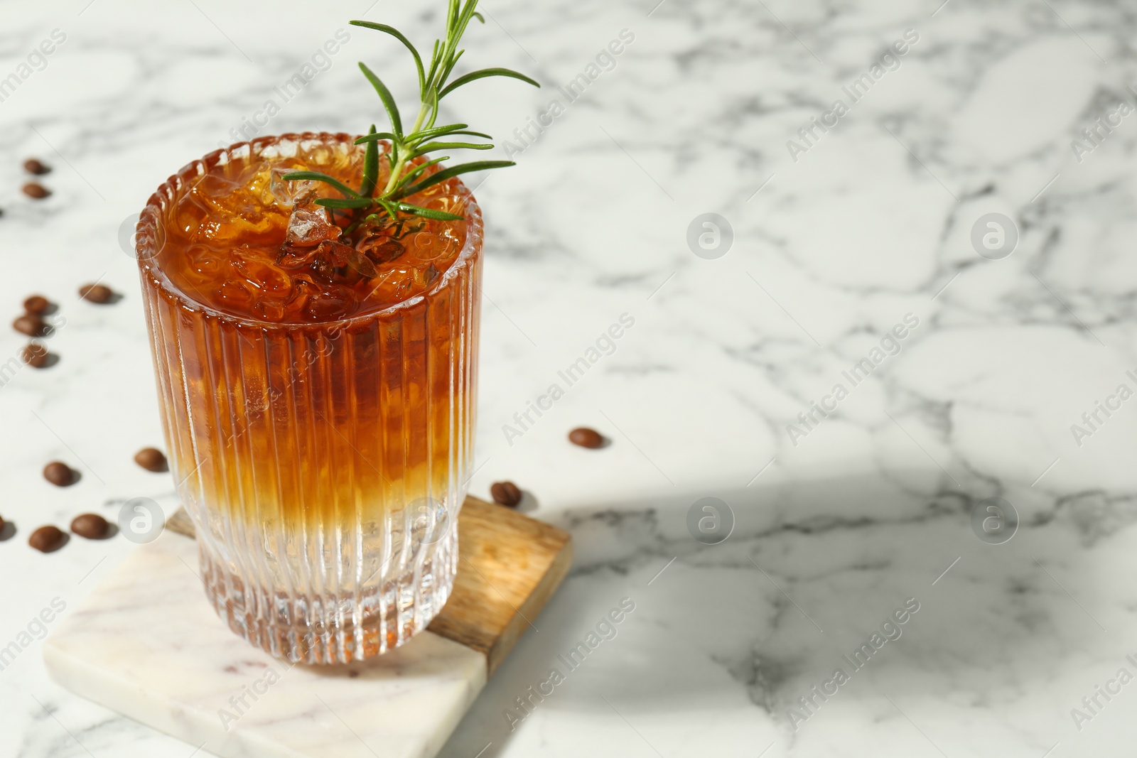 Photo of Refreshing espresso tonic drink with rosemary and coffee beans on white marble table, closeup. Space for text