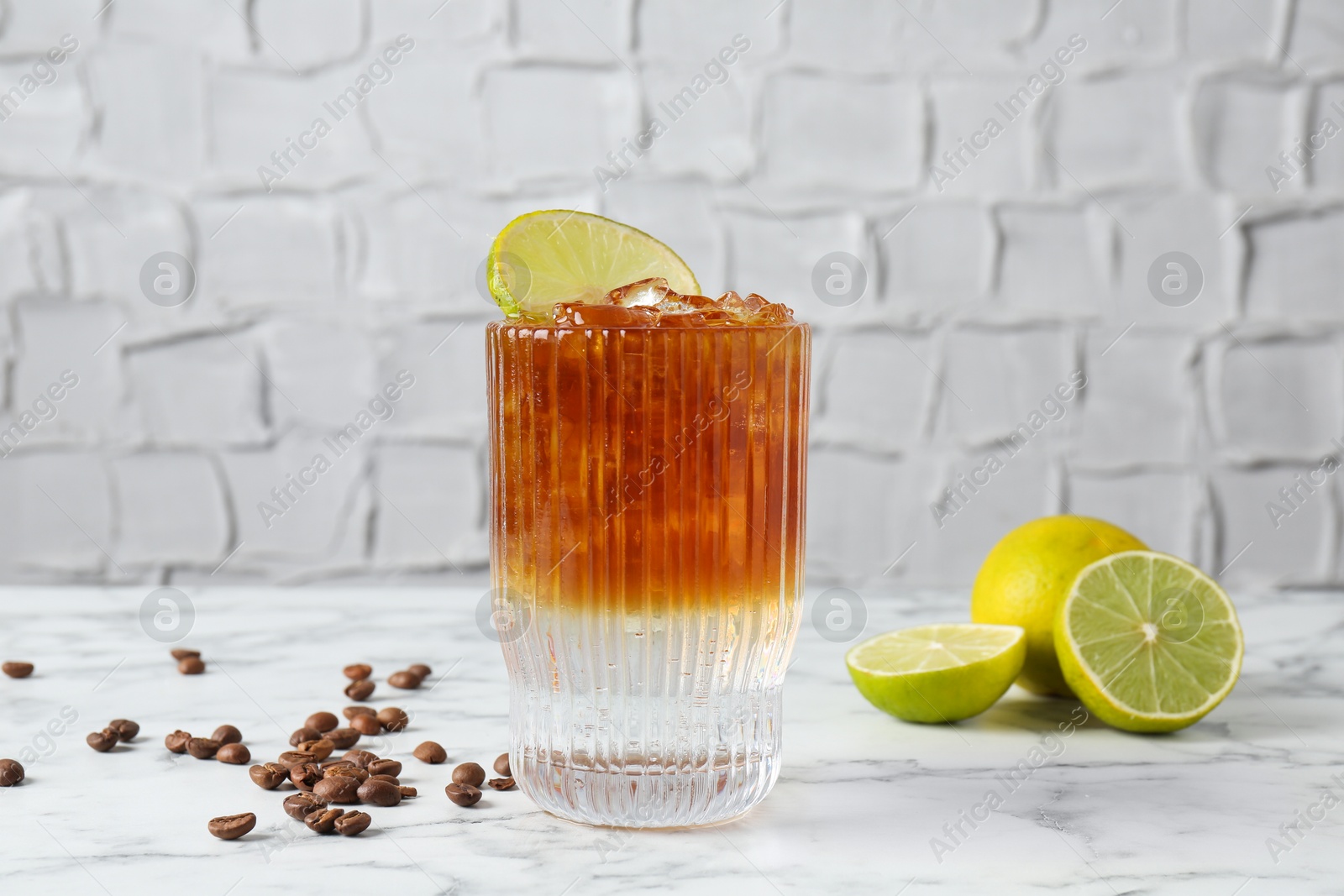 Photo of Refreshing espresso tonic drink with lime and coffee beans on white marble table