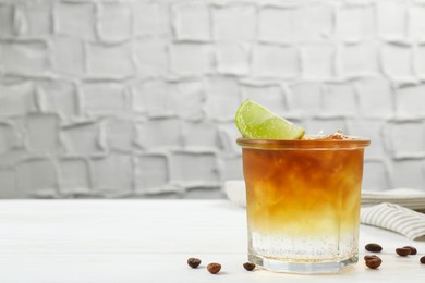 Photo of Refreshing espresso tonic drink with slice of lime and coffee beans on white wooden table, space for text