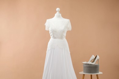 Photo of Mannequin with beautiful wedding dress and shoes on pale brown background