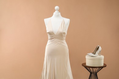 Photo of Mannequin with beautiful wedding dress and shoes on pale brown background