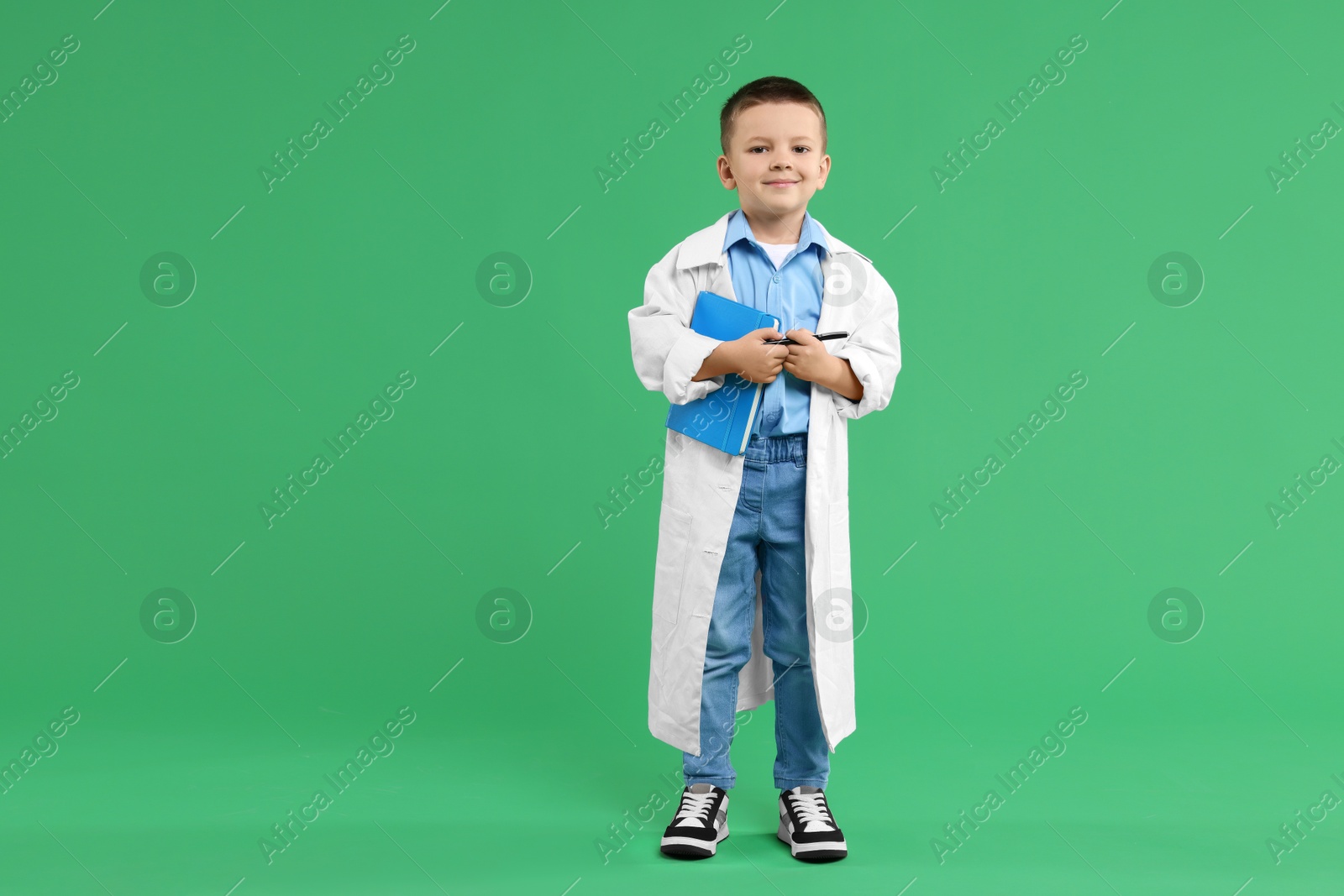 Photo of Little boy with book pretending to be doctor on green background, space for text. Dreaming of future profession