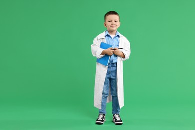 Photo of Little boy with book pretending to be doctor on green background, space for text. Dreaming of future profession