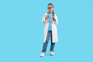 Photo of Girl with stethoscope pretending to be doctor on light blue background. Dreaming of future profession