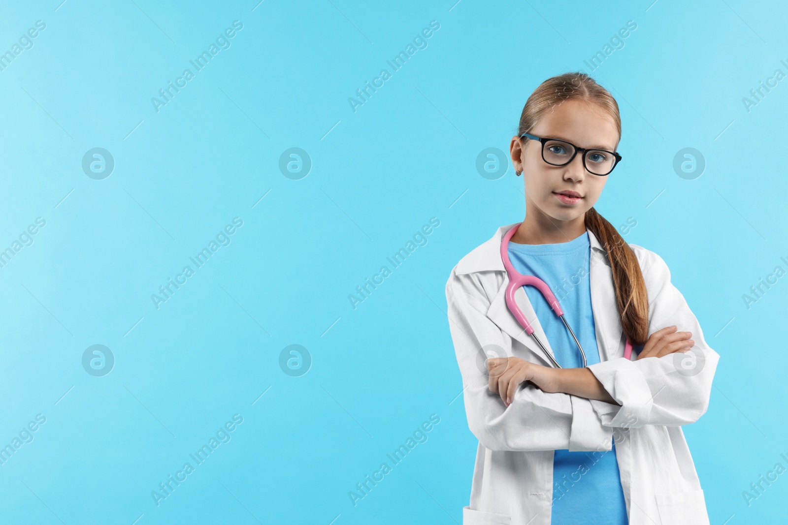 Photo of Girl with stethoscope pretending to be doctor on light blue background, space for text. Dreaming of future profession