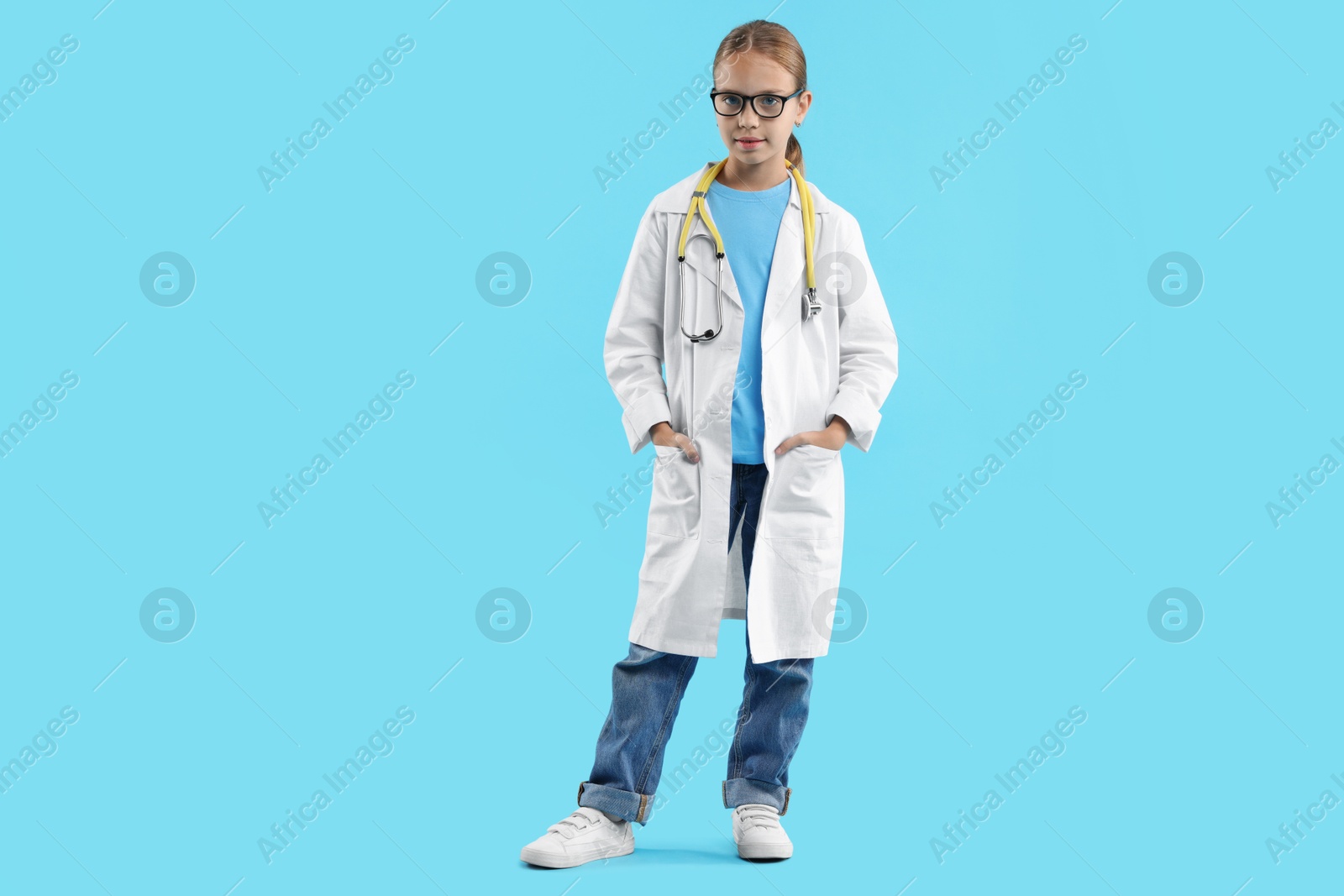 Photo of Girl with stethoscope pretending to be doctor on light blue background. Dreaming of future profession