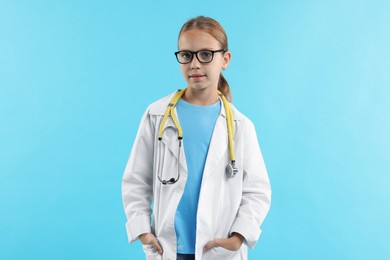 Photo of Girl with stethoscope pretending to be doctor on light blue background. Dreaming of future profession