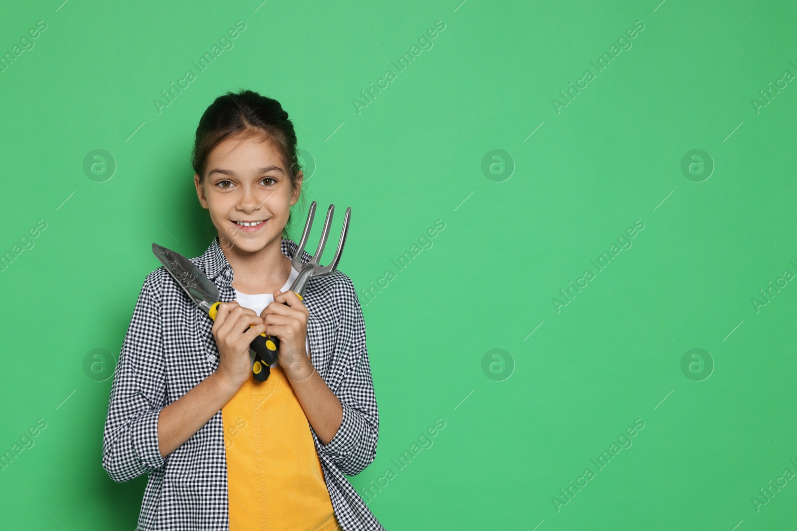 Photo of Girl with tools pretending to be gardener on green background, space for text. Dreaming of future profession