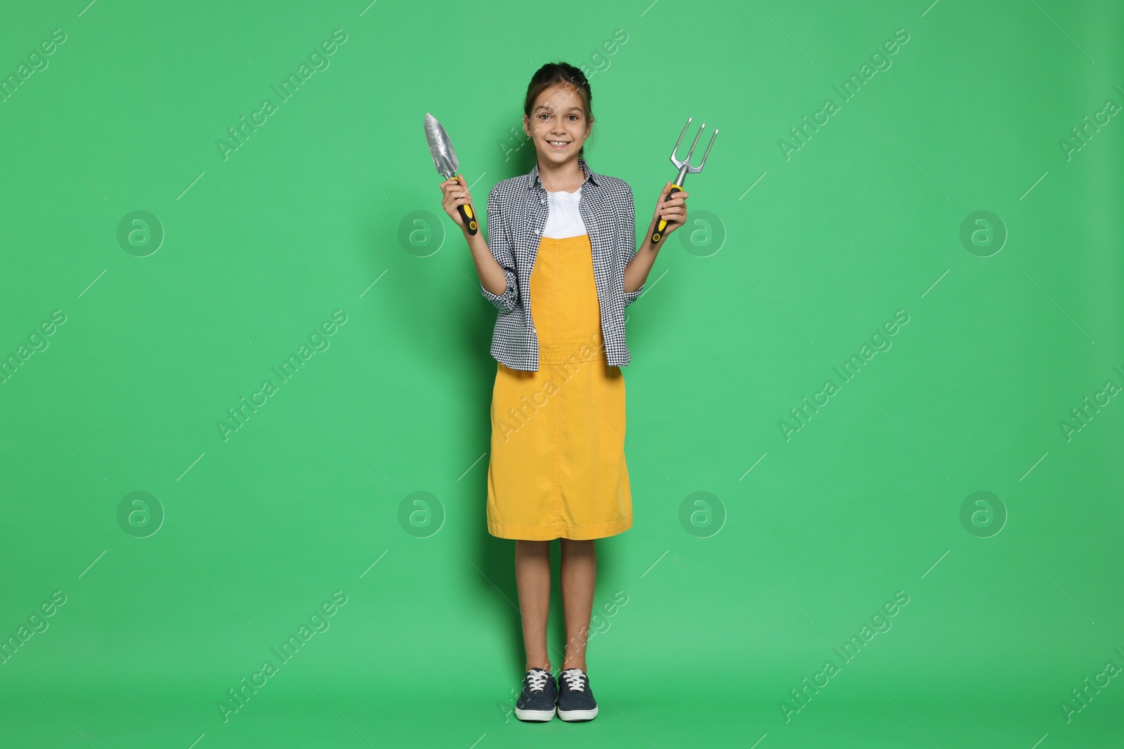 Photo of Girl with tools pretending to be gardener on green background. Dreaming of future profession