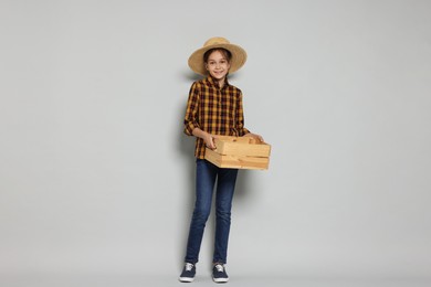 Girl with straw hat and wooden crate pretending to be farmer on light grey background. Dreaming of future profession