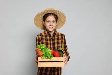 Photo of Girl with straw hat, wooden crate and vegetables pretending to be farmer on light grey background. Dreaming of future profession