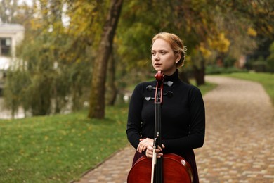 Photo of Beautiful young woman with cello in park, space for text