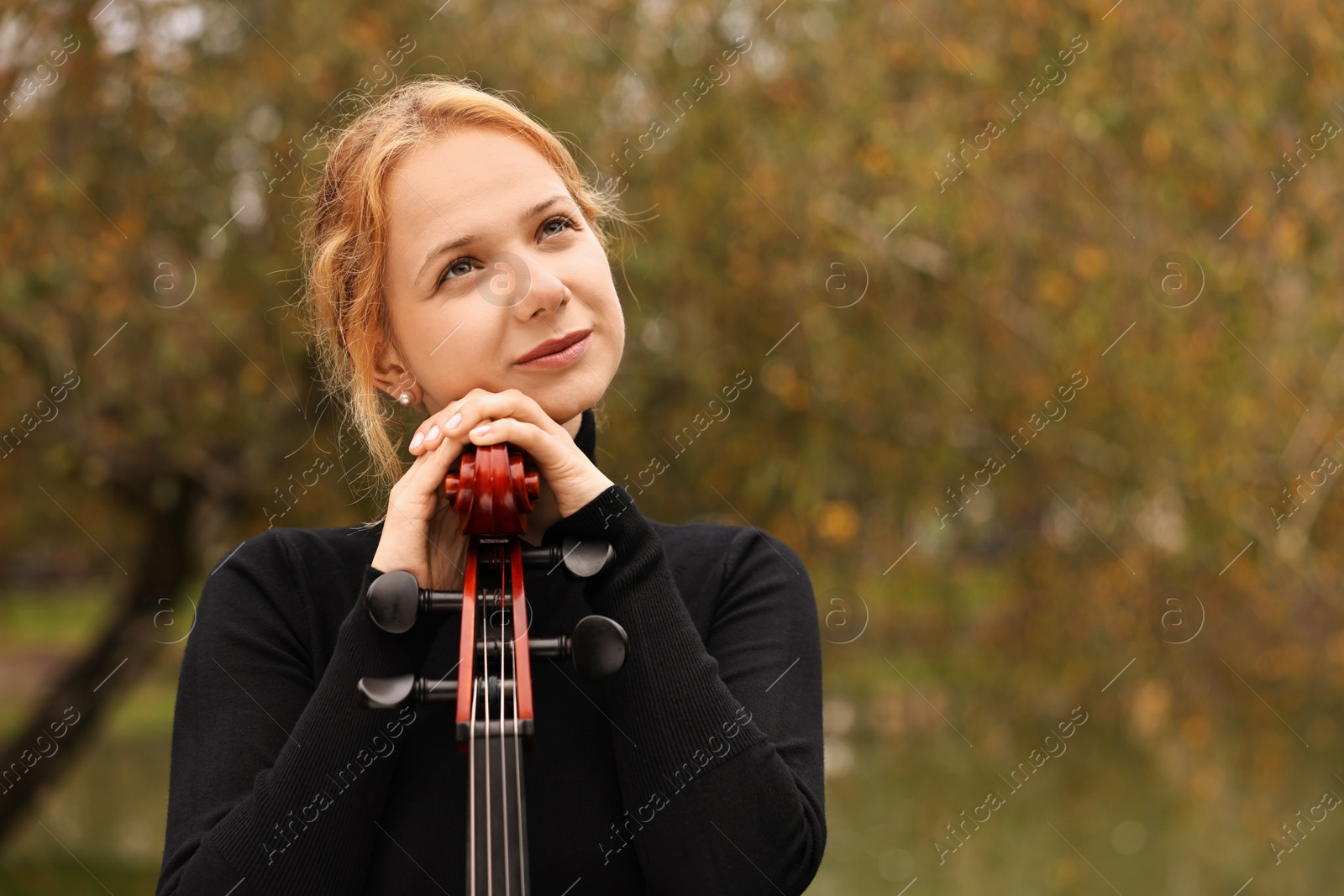 Photo of Beautiful young woman with cello in park, space for text