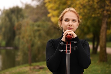 Photo of Beautiful young woman with cello in park, space for text