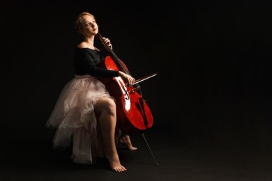 Photo of Beautiful young woman with cello on black background, space for text