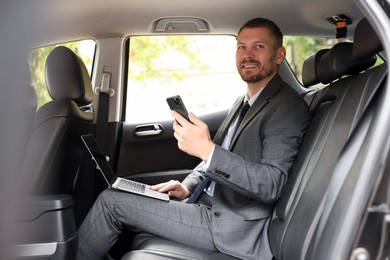 Photo of Man with laptop and smartphone in modern car