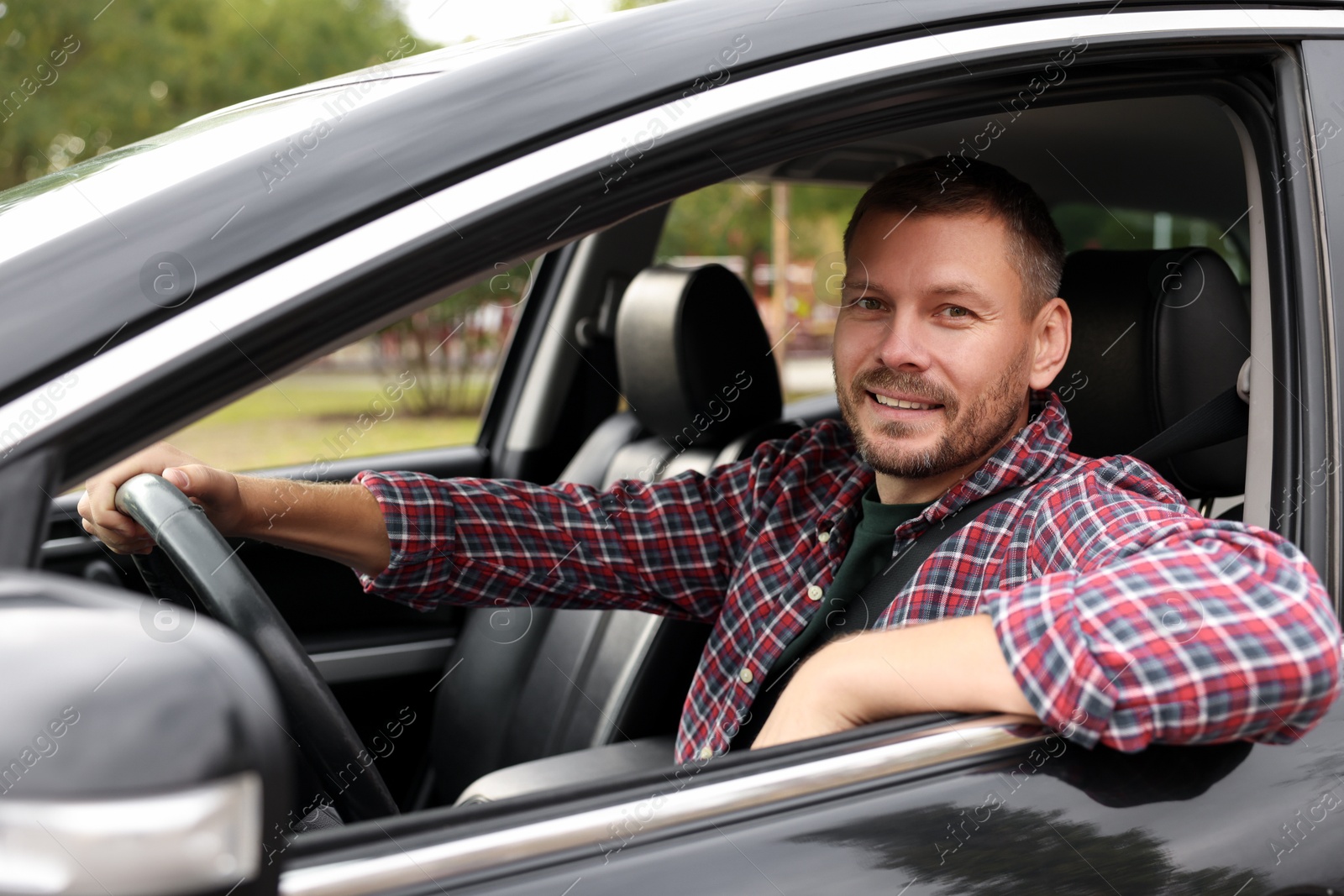 Photo of Happy man behind steering wheel of modern car, view from outside