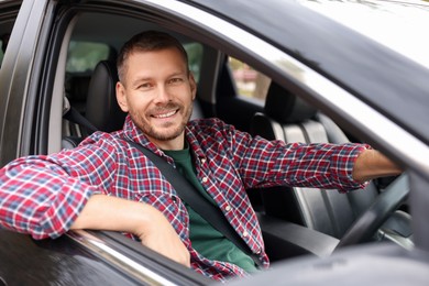 Photo of Happy man behind steering wheel of modern car, view from outside