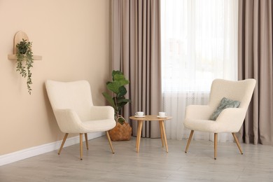 Photo of Soft armchairs and coffee table near beige wall indoors