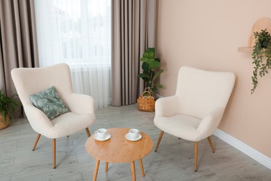 Photo of Soft armchairs and coffee table near beige wall indoors