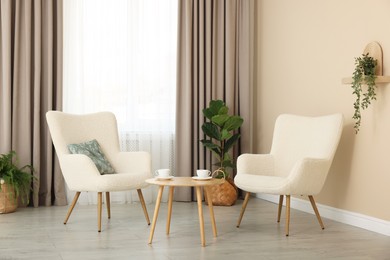 Soft armchairs and coffee table near beige wall indoors