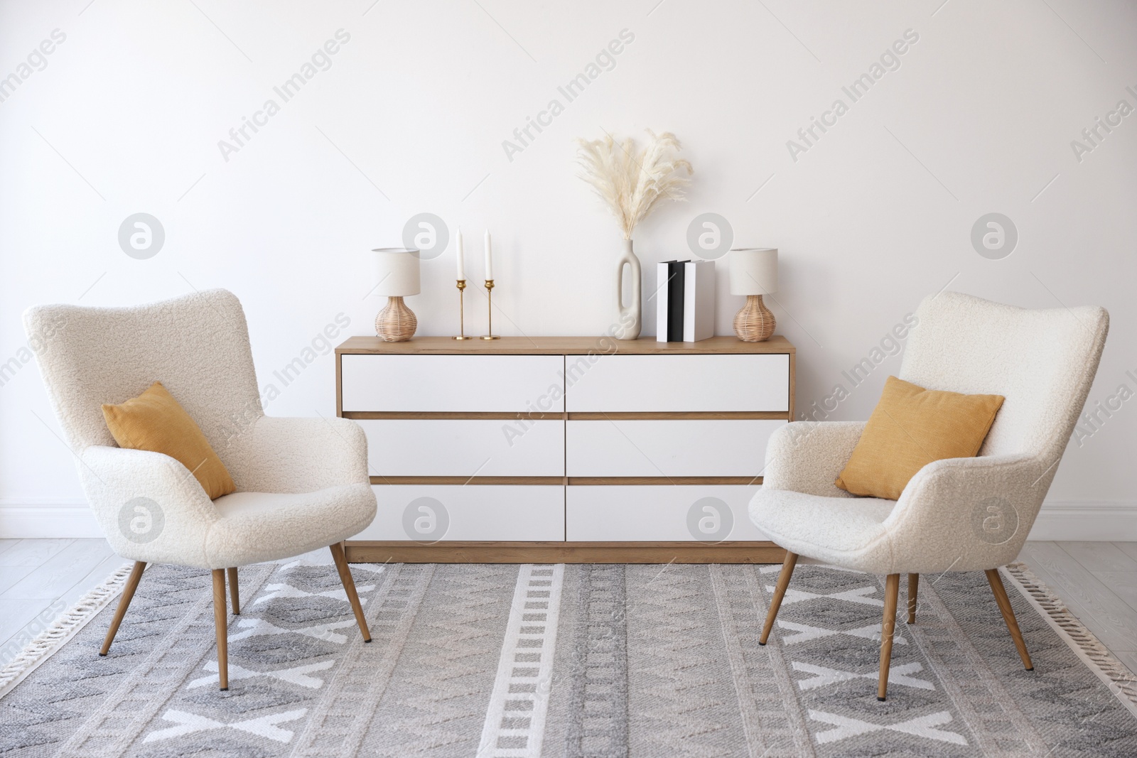 Photo of Soft armchairs and chest of drawers near white wall indoors