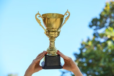 Woman holding golden trophy against blue sky outdoors, closeup