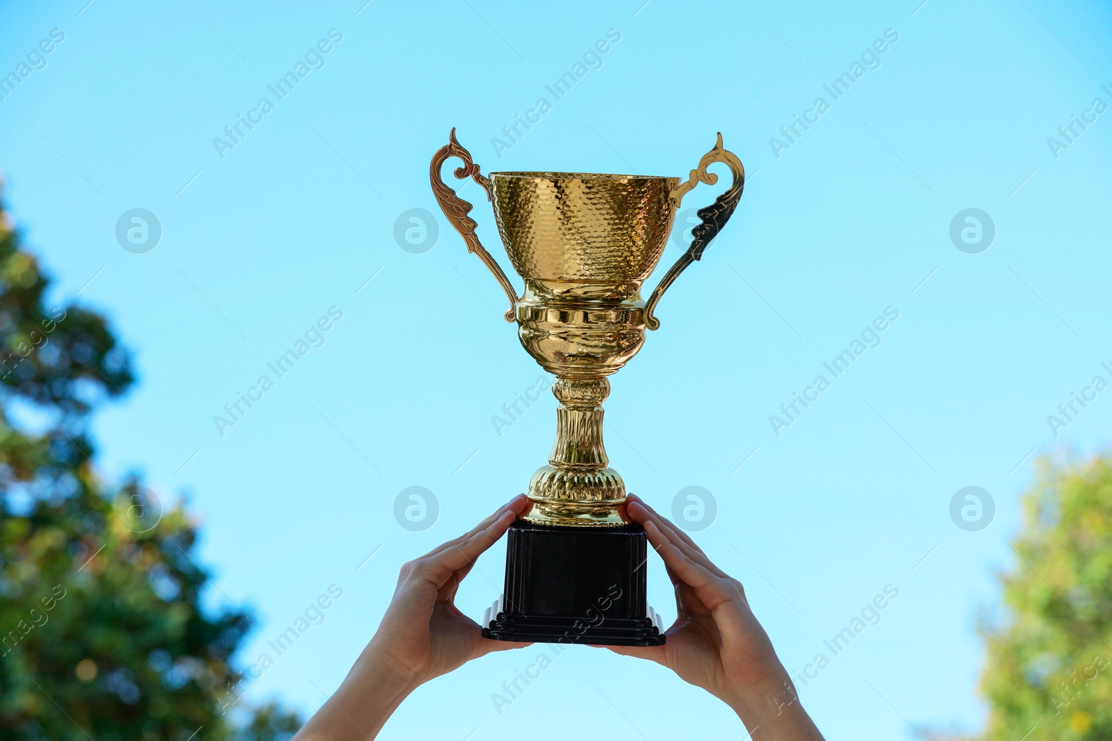 Photo of Woman holding golden trophy against blue sky outdoors, closeup