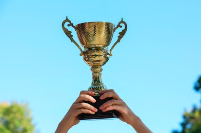 Photo of Woman holding golden trophy against blue sky outdoors, closeup