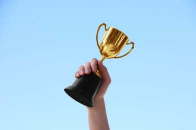 Photo of Woman holding golden trophy against blue sky outdoors, closeup