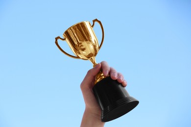 Woman holding golden trophy against blue sky outdoors, closeup