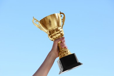 Photo of Woman holding golden trophy against blue sky outdoors, closeup