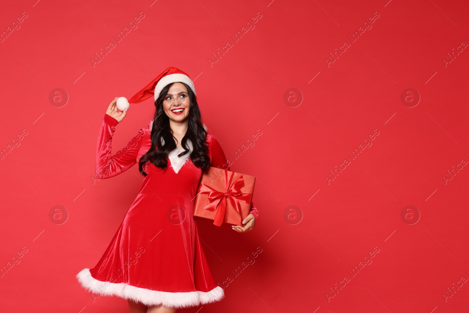 Photo of Beautiful woman in Mrs Claus costume with Christmas gift on red background, space for text