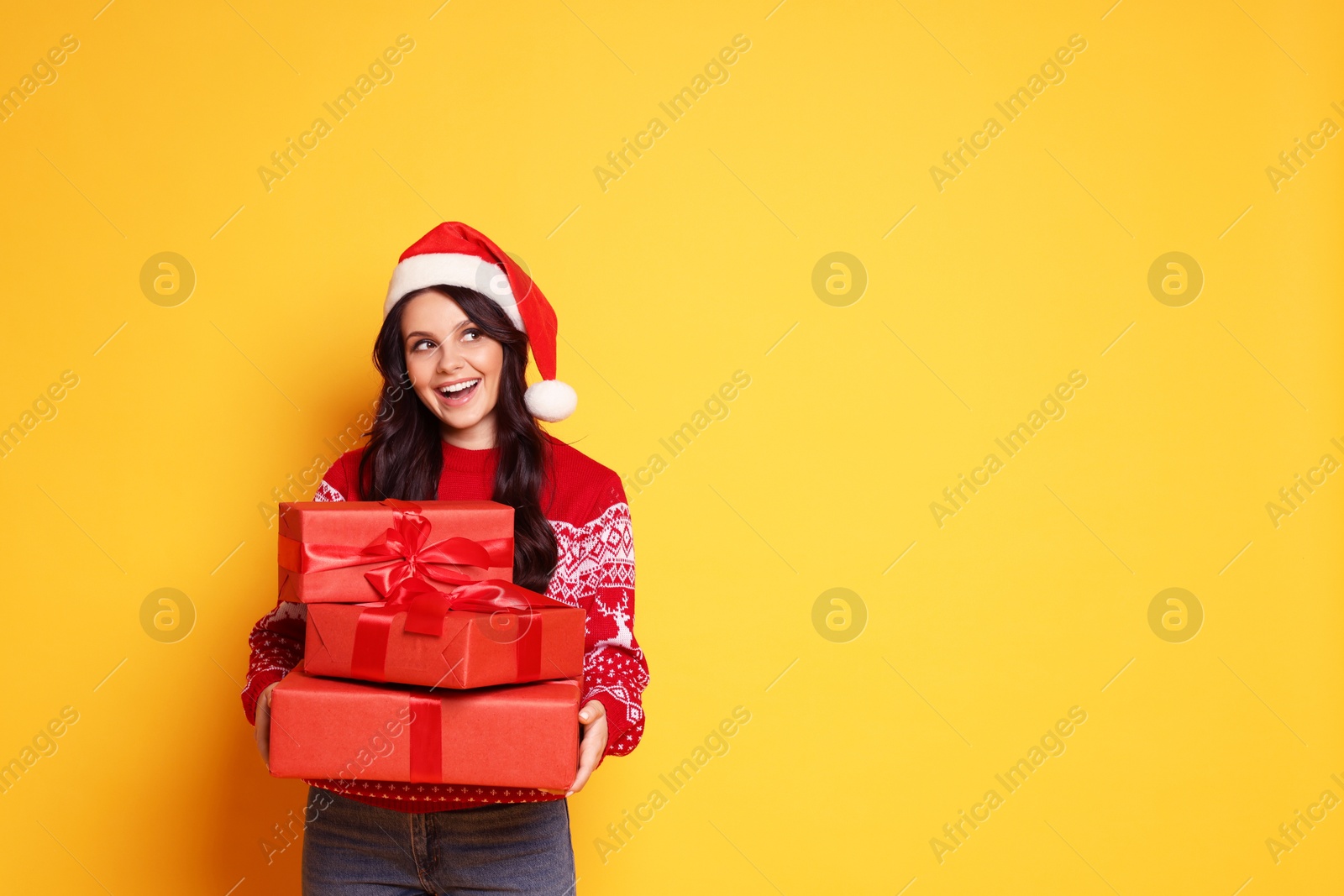 Photo of Woman in Santa hat with Christmas gifts on yellow background, space for text