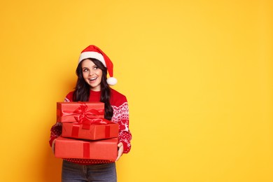 Photo of Woman in Santa hat with Christmas gifts on yellow background, space for text