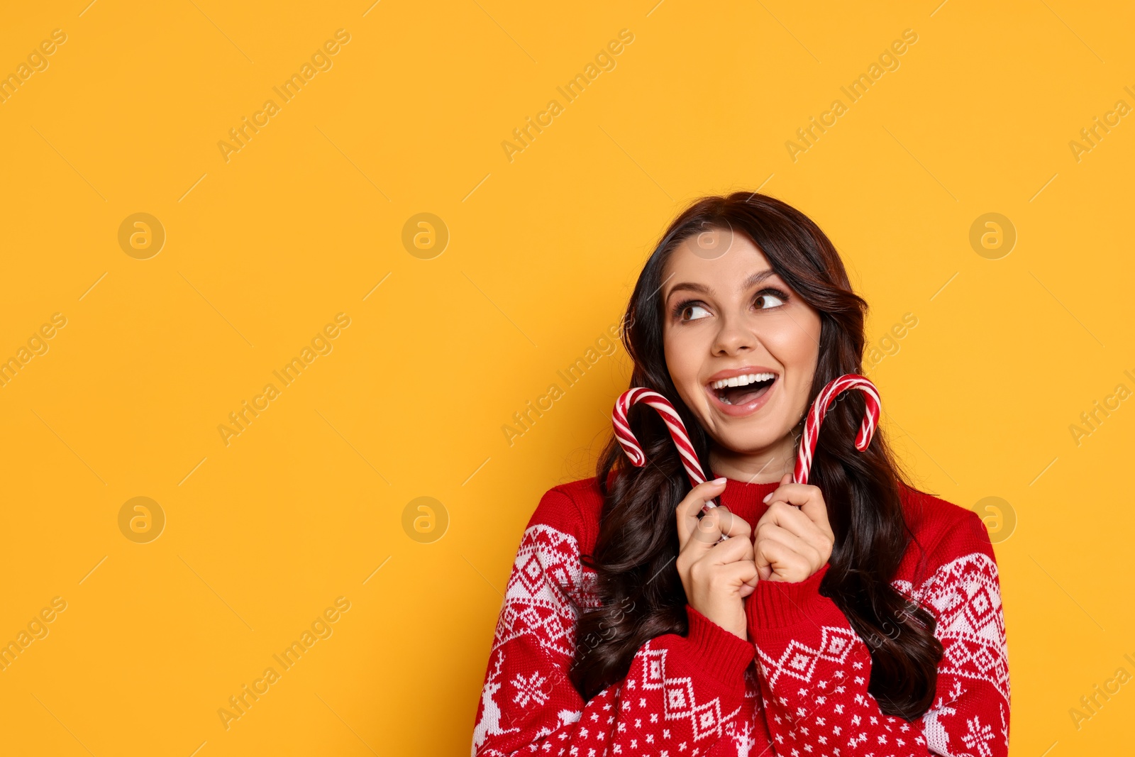 Photo of Excited woman in Christmas sweater with candy canes on yellow background, space for text