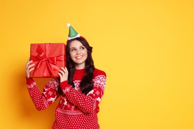 Photo of Happy woman with Christmas gift on yellow background, space for text