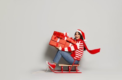 Woman with Christmas gifts on sledge against light grey background