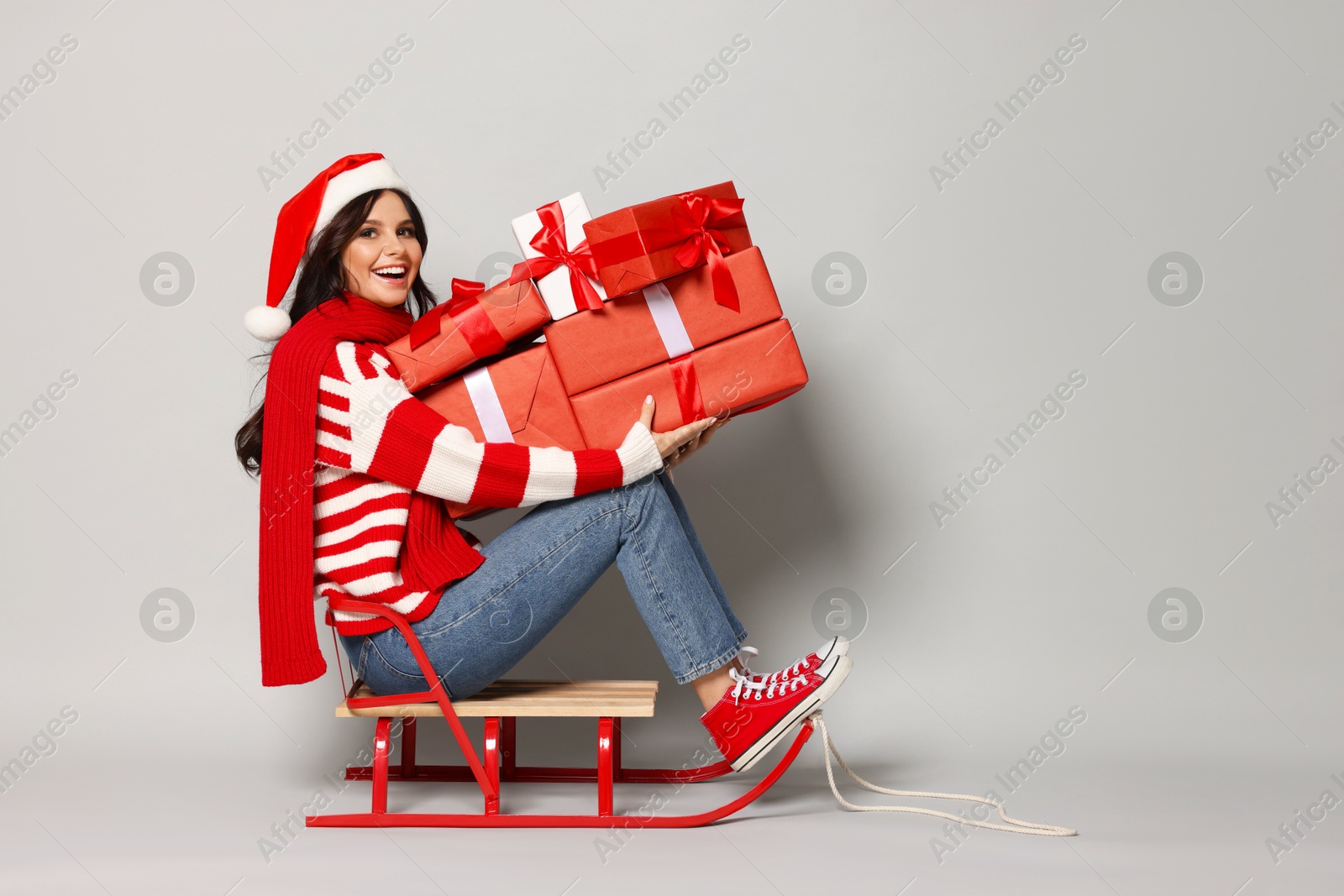 Photo of Woman with Christmas gifts on sledge against light grey background