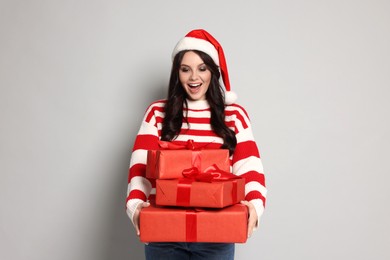 Photo of Woman in Santa hat with Christmas gifts on light grey background