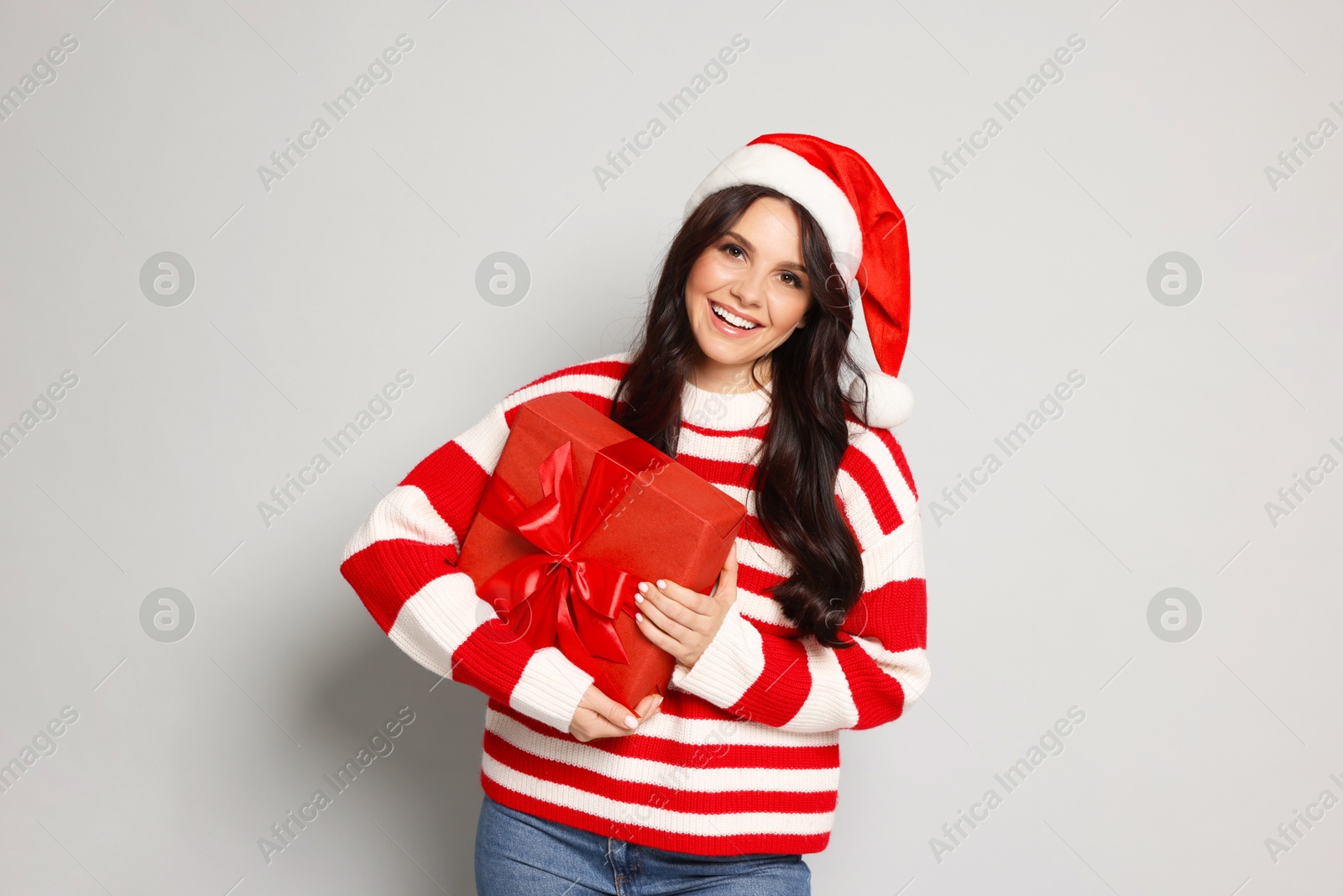 Photo of Woman in Santa hat with Christmas gift on light grey background