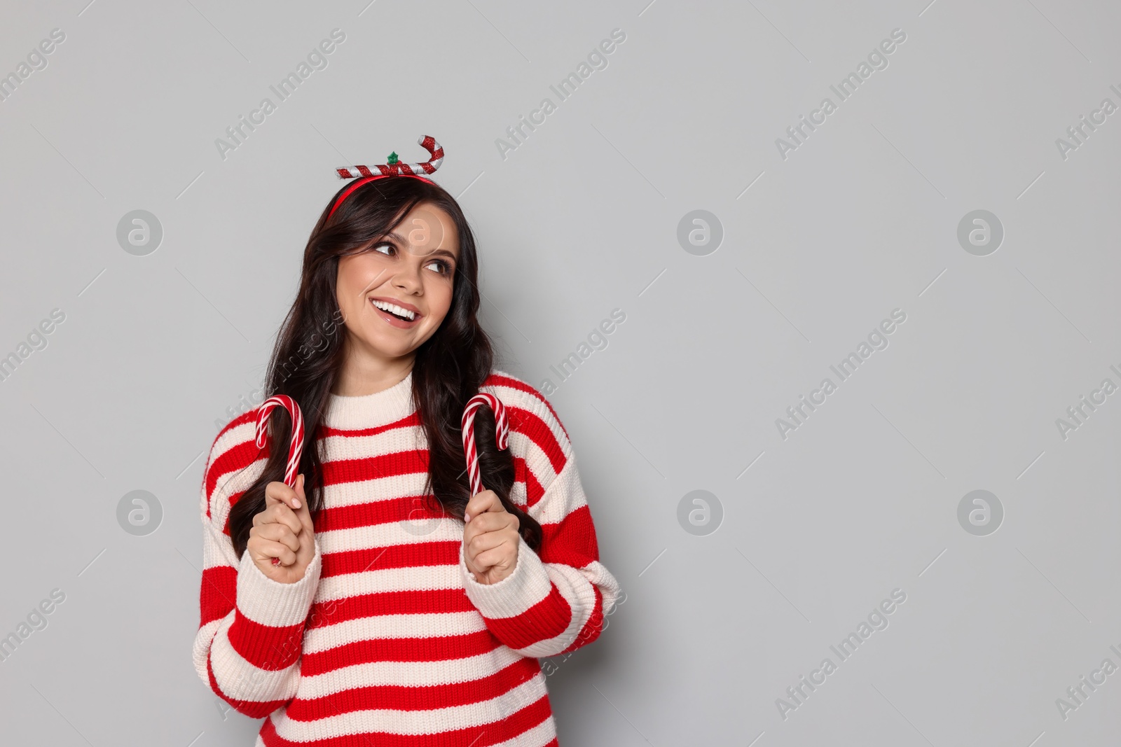 Photo of Happy woman with candy canes on light grey background, space for text. Christmas celebration