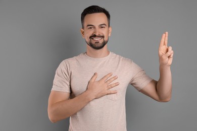 Photo of Man showing oath gesture on grey background. Making promise