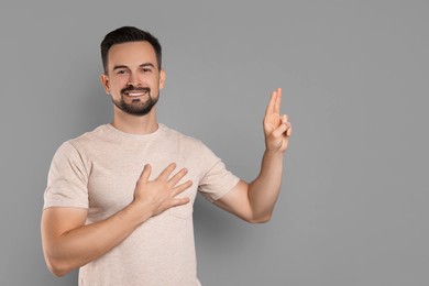 Photo of Man showing oath gesture on grey background, space for text. Making promise