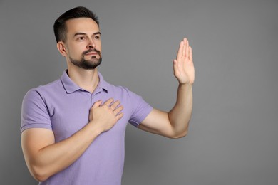 Photo of Man making promise with raised hand on grey background, space for text. Oath gesture