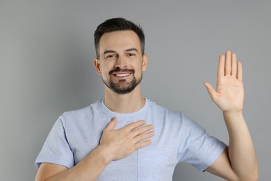 Photo of Man making promise with raised hand on grey background. Oath gesture