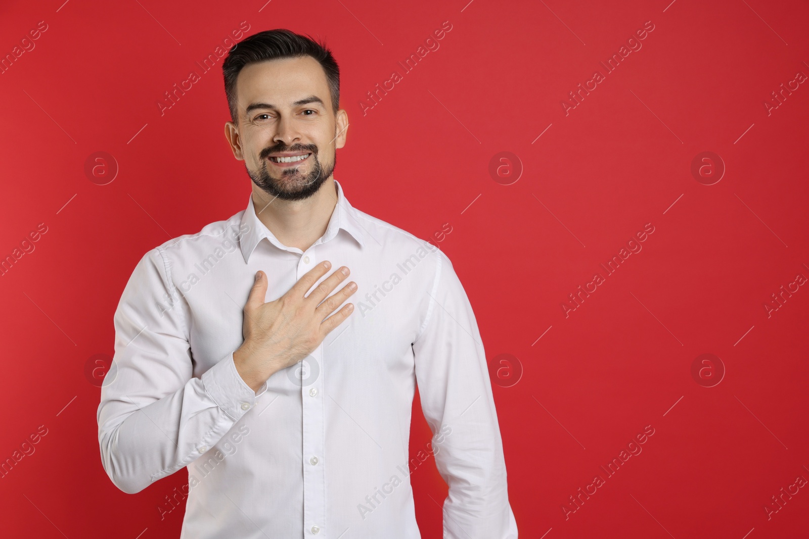 Photo of Man making promise on red background, space for text. Oath gesture