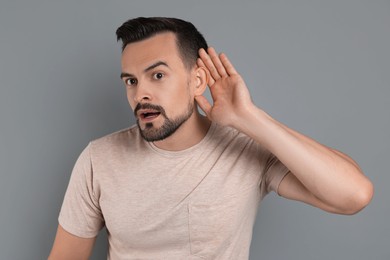 Photo of Man showing hand to ear gesture on grey background